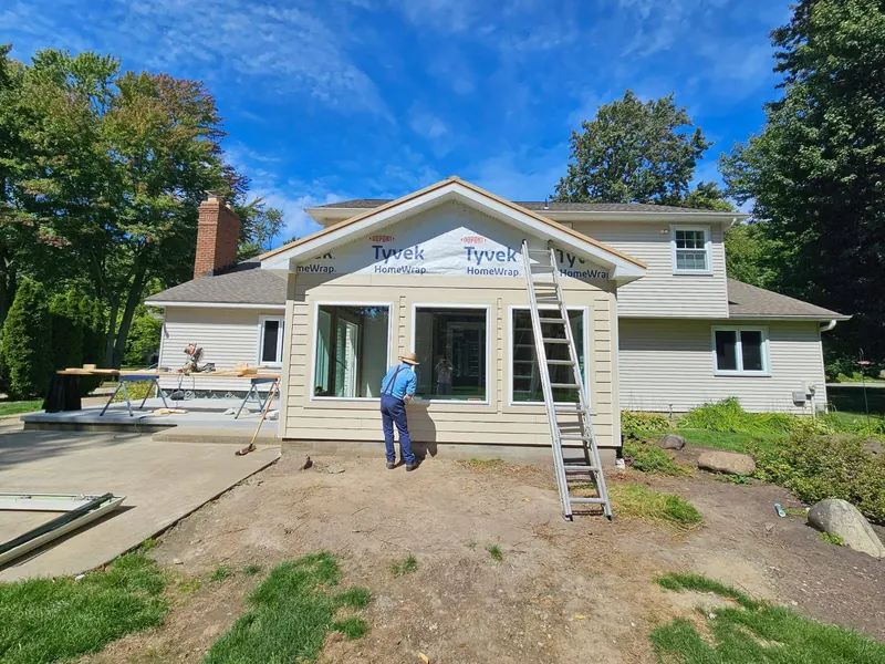 Home addition wrapped in weather barrier with a crew member working beside a ladder