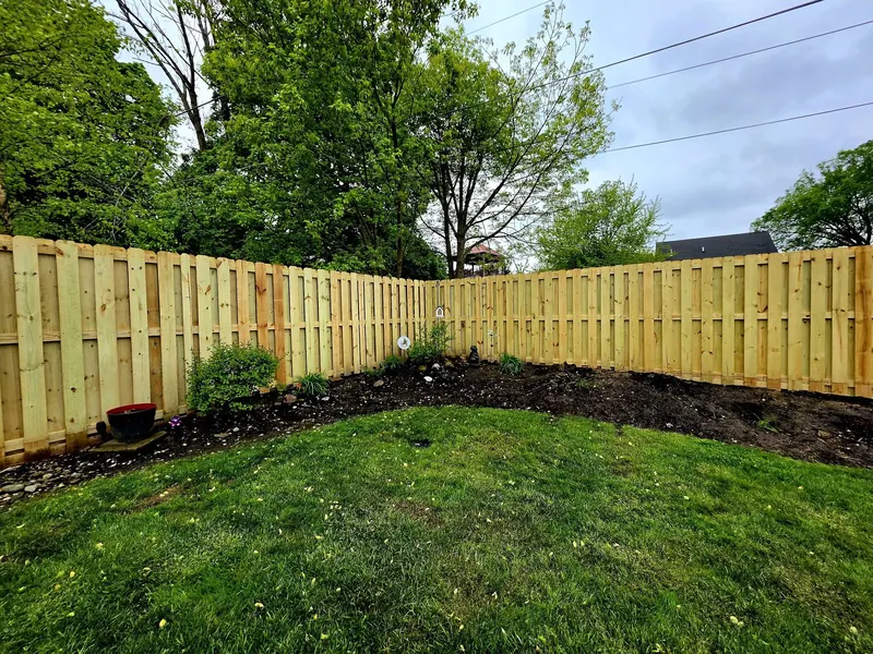 Long run of new wood privacy fence curving around a lawn and garden bed