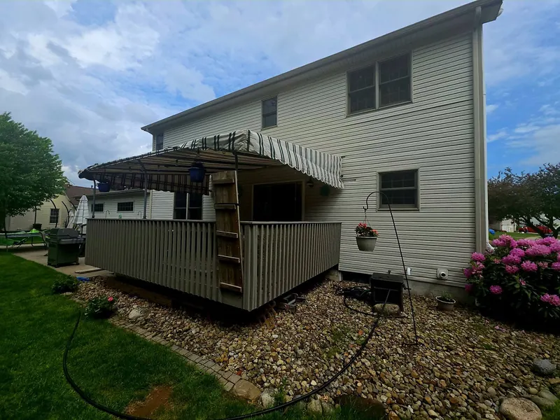 Backyard deck with railing and a striped awning attached to a two-story home