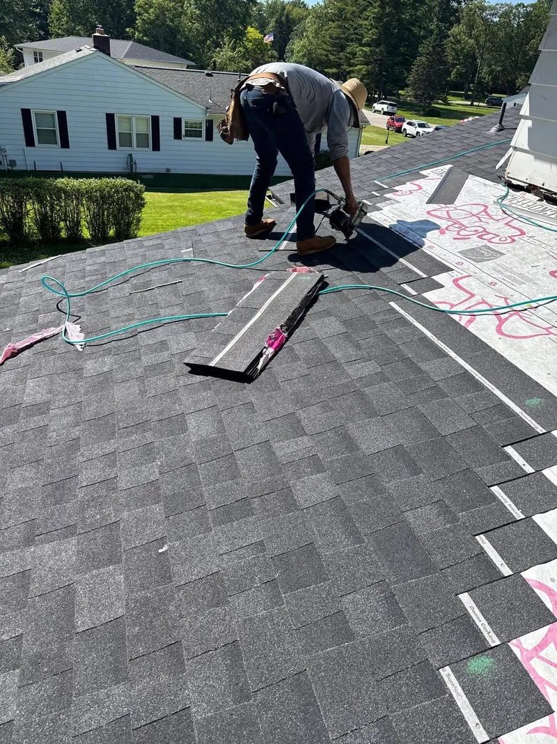 Roofer kneeling on a pitched roof while installing dark architectural shingles