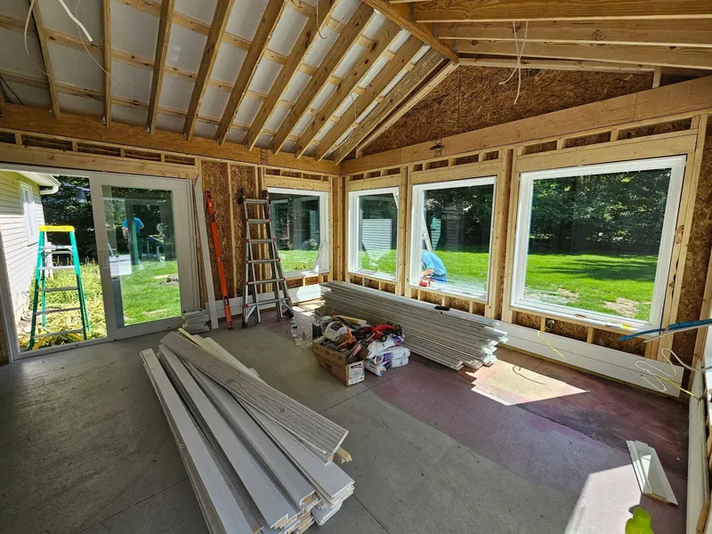 Gable-roofed addition interior framed with large new windows and siding stacked on the floor