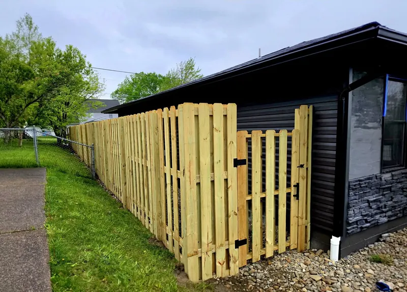 New wood fence with a gate running along the side of a home with dark siding and stone veneer